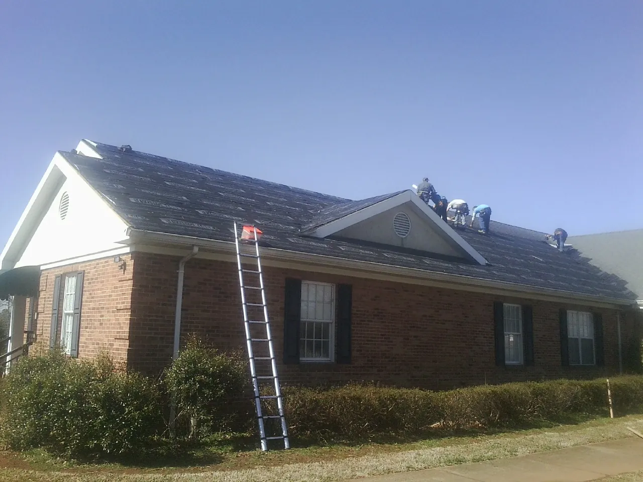 Crew tearing shingles off a brick ranch roof with a ladder set — Metal Roof Repair work by our crew in Dewar