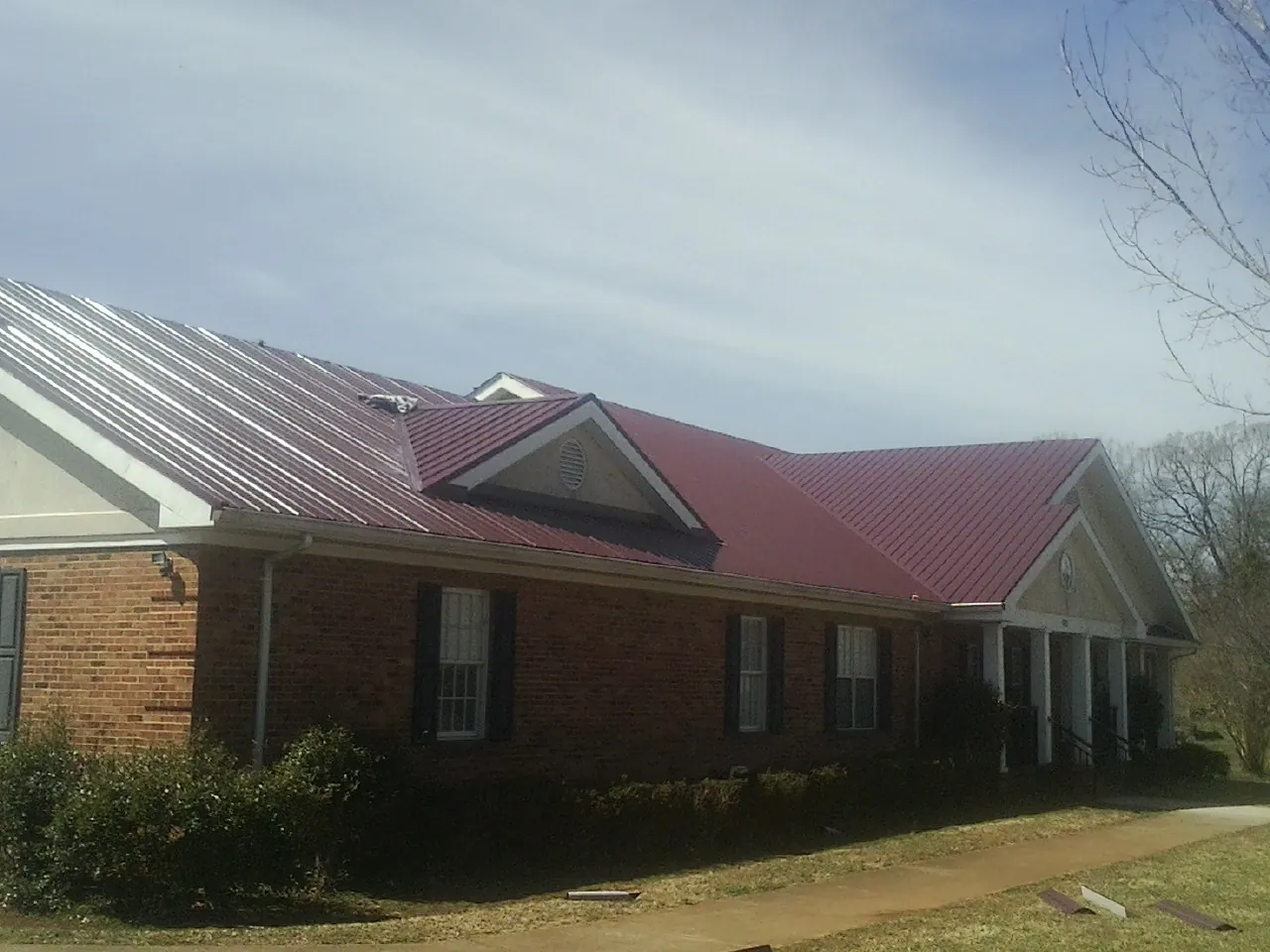 Red metal roof with gabled entries on a long brick building, from a Hail Damage Roof Repair job in Dewar