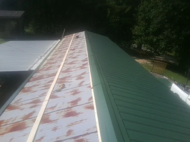 Old rusted panels beside newly installed green metal roofing — Wind Damage Roof Repair by Roofing Brothers in Dewar