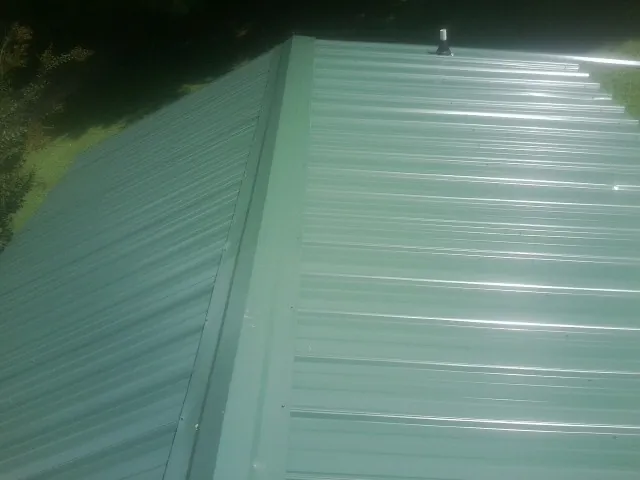 New green metal panels meeting at the ridge of a roof — Flat Roof Repair work by our crew in Dewar