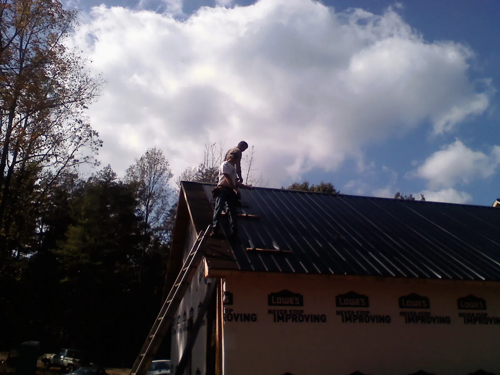 Roofer fastening dark metal panels high against a cloudy sky, from a Roof Inspection job in Dewar