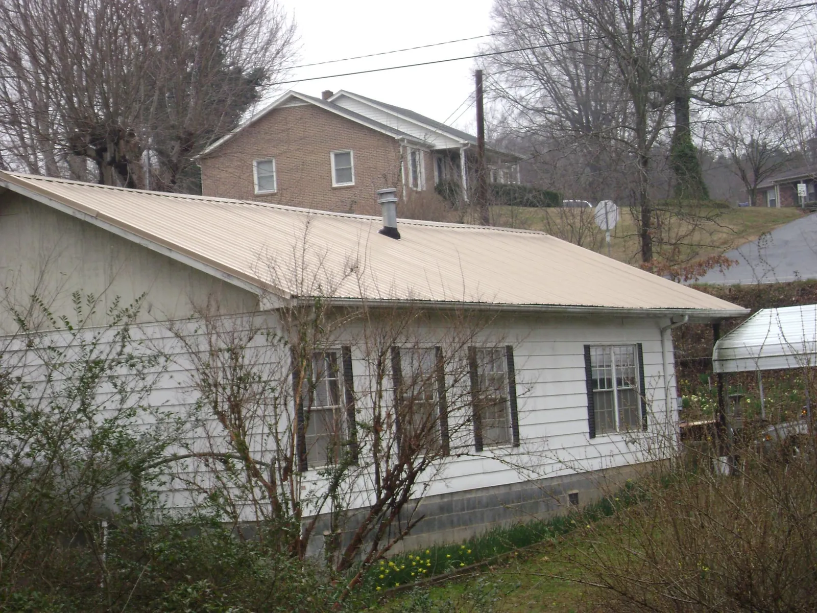 Tan metal roof on a white sided house set into a hillside — Commercial Roofing by Roofing Brothers in Dewar