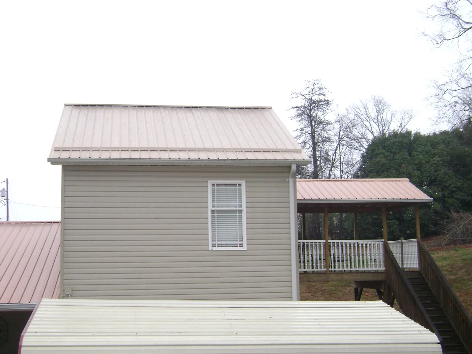 Tan metal roofs on a two story addition and attached porch, from a Roof Replacement job in Dewar