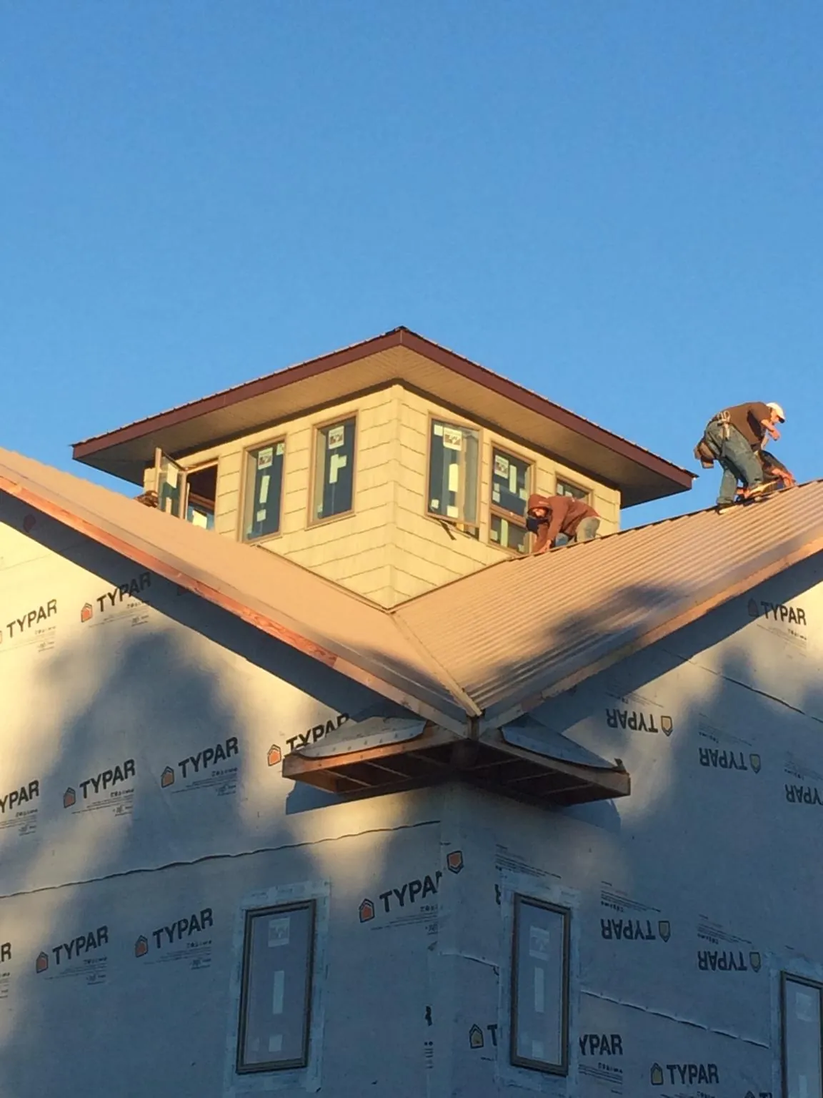 Roofers working around a rooftop cupola on a new metal roof at sunset — Roof Waterproofing in Dewar by Roofing Brothers